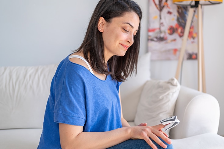 Woman Using Pulse Oximeter On Couch